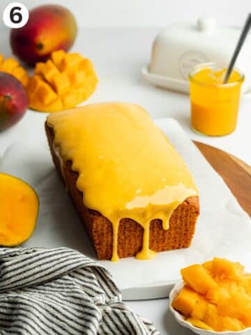 mango loaf cake on a sheet of parchment paper with mango glaze poured over the top.