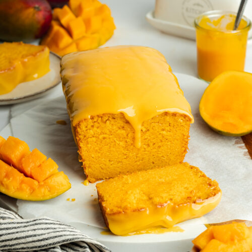 vibrant mango loaf cake with mango icing on top and a slice cut showing the moist interior.