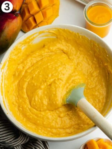 mango cake batter in a ceramic bowl with a rubber spatula.