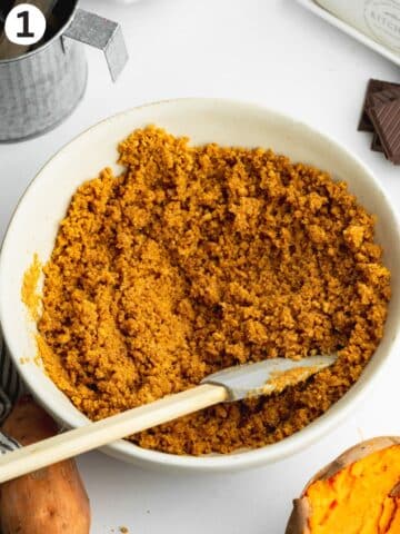 cookie crumbs mixed with melted butter with a spatula in a large ceramic bowl.