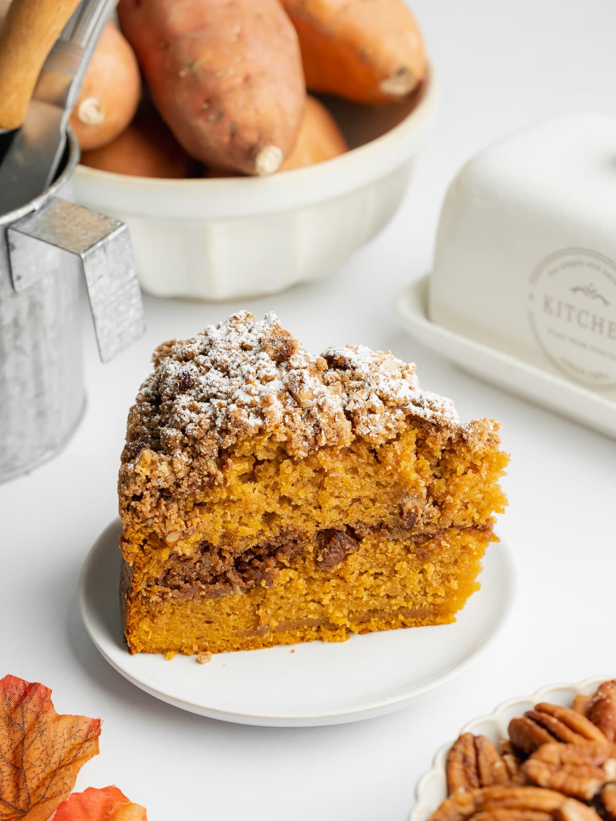 a slice of sweet potato coffee cake with cinnamon crumb topping on a white plate with a bowl of sweet potatoes in the background.