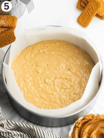 a thin layer of biscoff cake batter in a lined cake pan.
