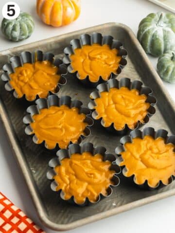 mini flan molds on a tray filled with pumpkin flan filling before setting.