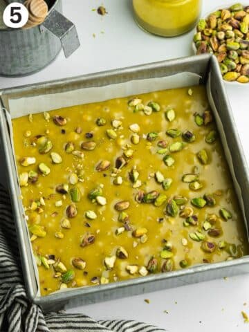 pistachio fudge in a lined tray with pistachio pieces on top before going into the fridge to set.