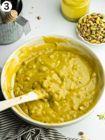 pistachio fudge mixture melted in a large bowl with pistachio pieces being folded through with a rubber spatula.