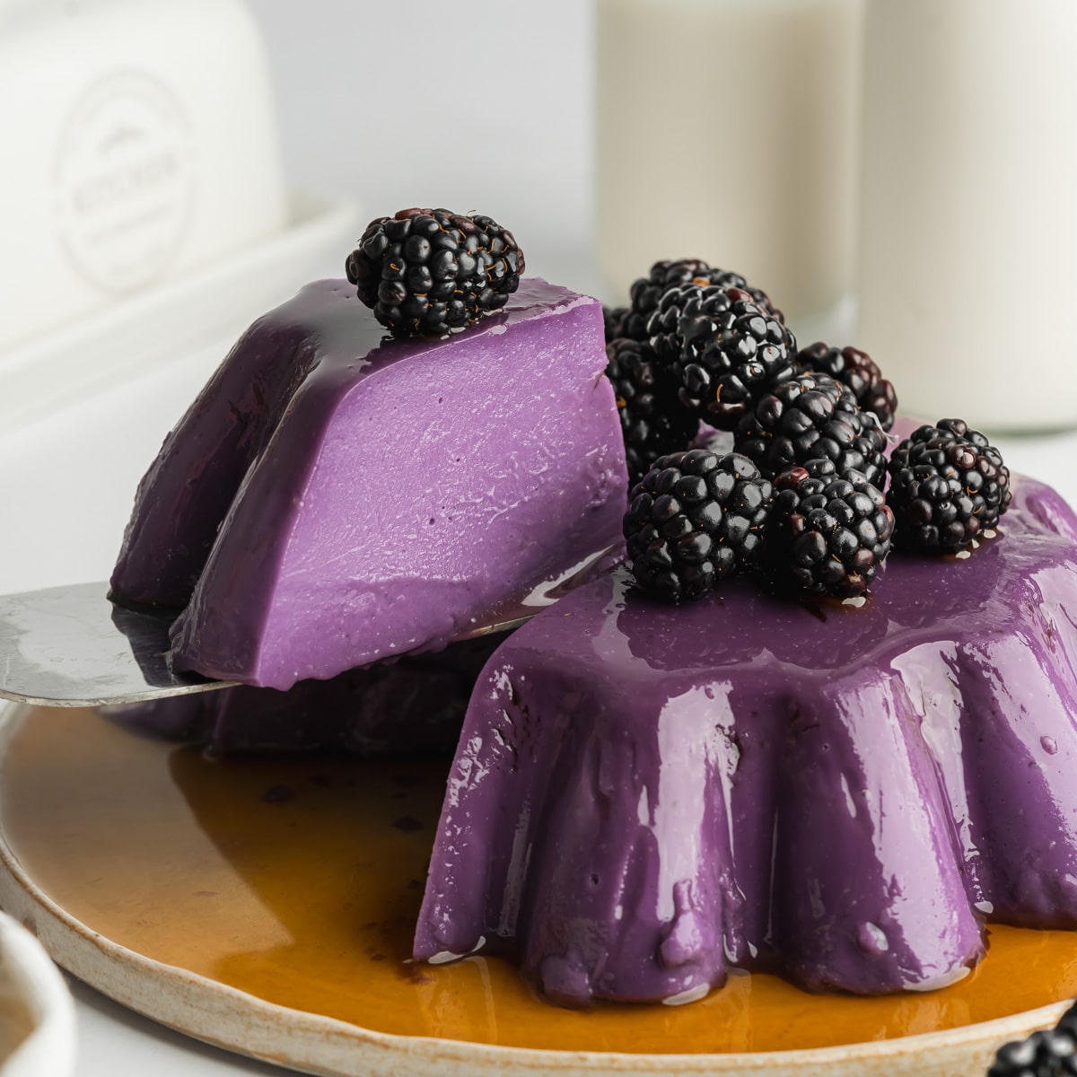 ube flan with blackberries on top and a slice being lifted away.