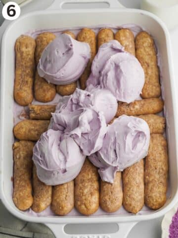 layered tiramisu in a white staub dish with dollops of purple mascarpone cream on top before being spread.