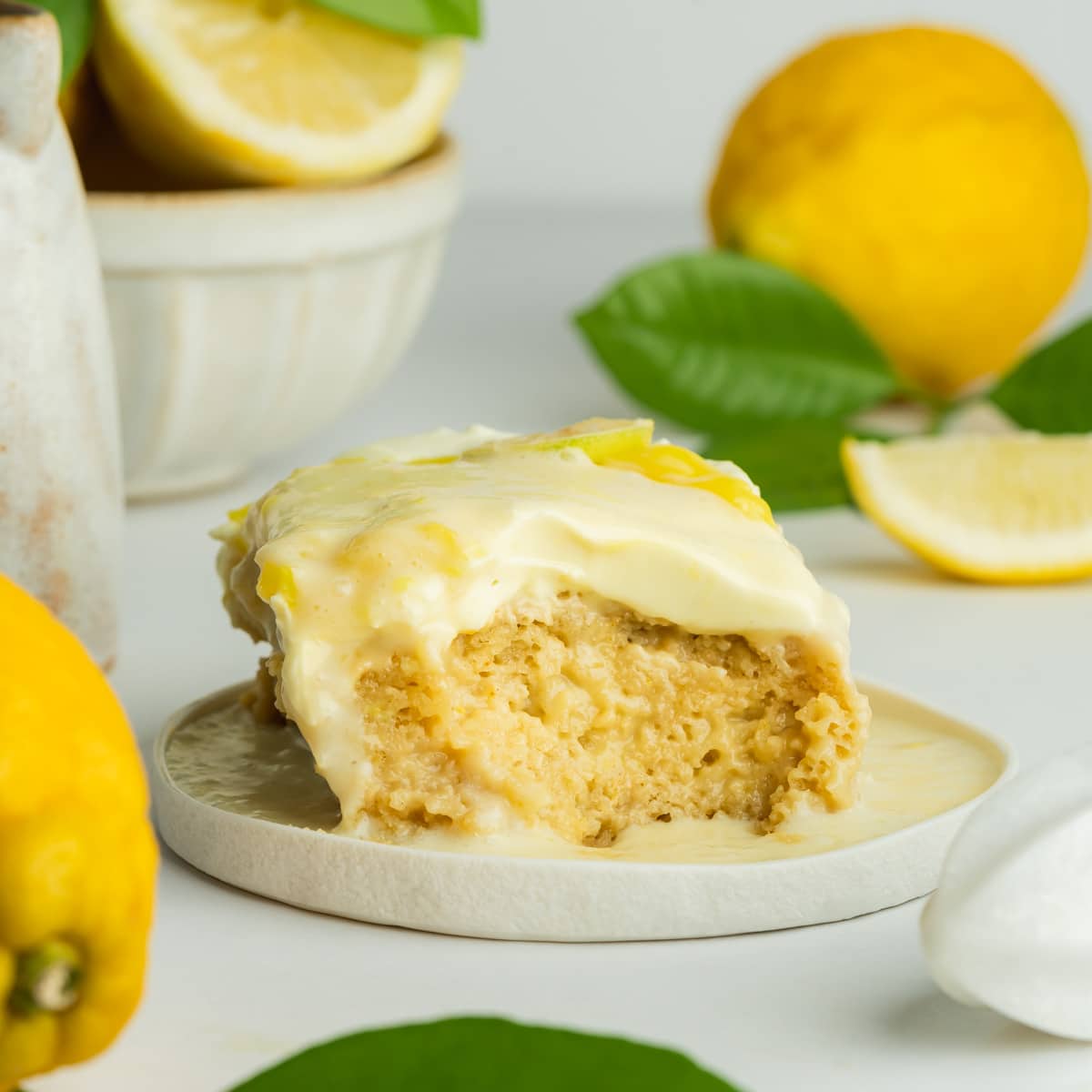 a slice of lemon tres leches with a spoonful taken, showing the moist consistency. There are fresh lemons scattered around the plate.