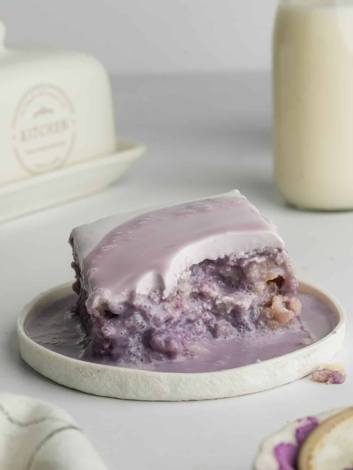 a slice of ube tres leches with a bite taken from it on a small white ceramic plate.