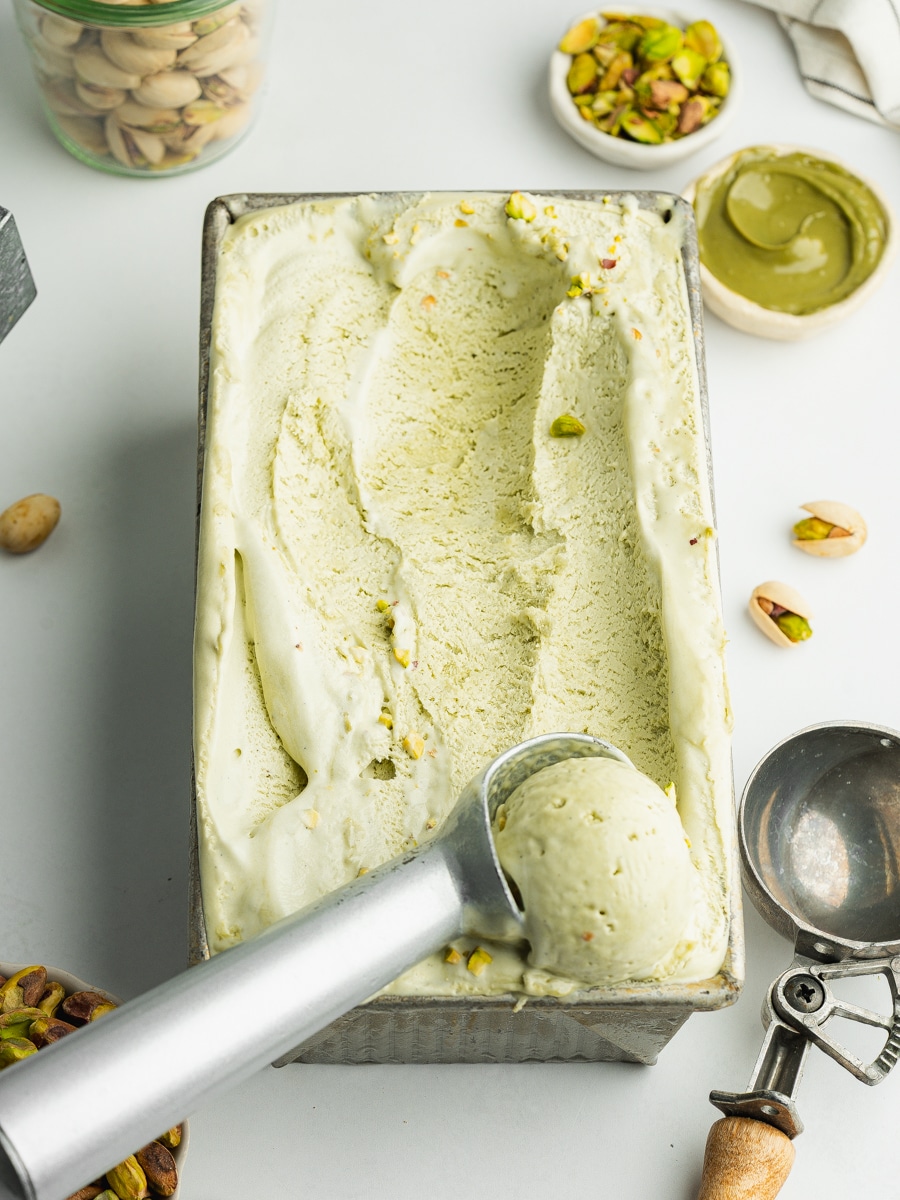 no churn pistachio ice cream in a loaf pan with a scoop in an ice cream scoop.