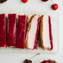 sliced of cherry cheesecake with cherry curd topping and fresh cherries scattered around.