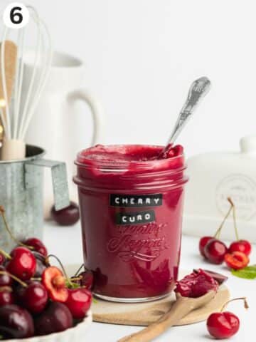 a jar of cherry curd with fresh cherries around it.