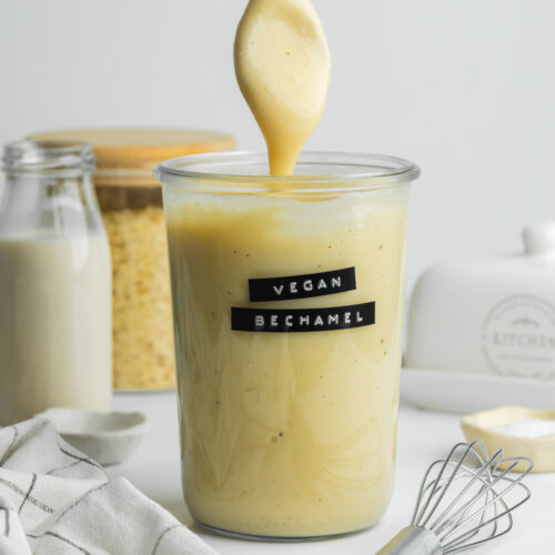 a jar of vegan bechamel with a spoon showing the thick consistency.