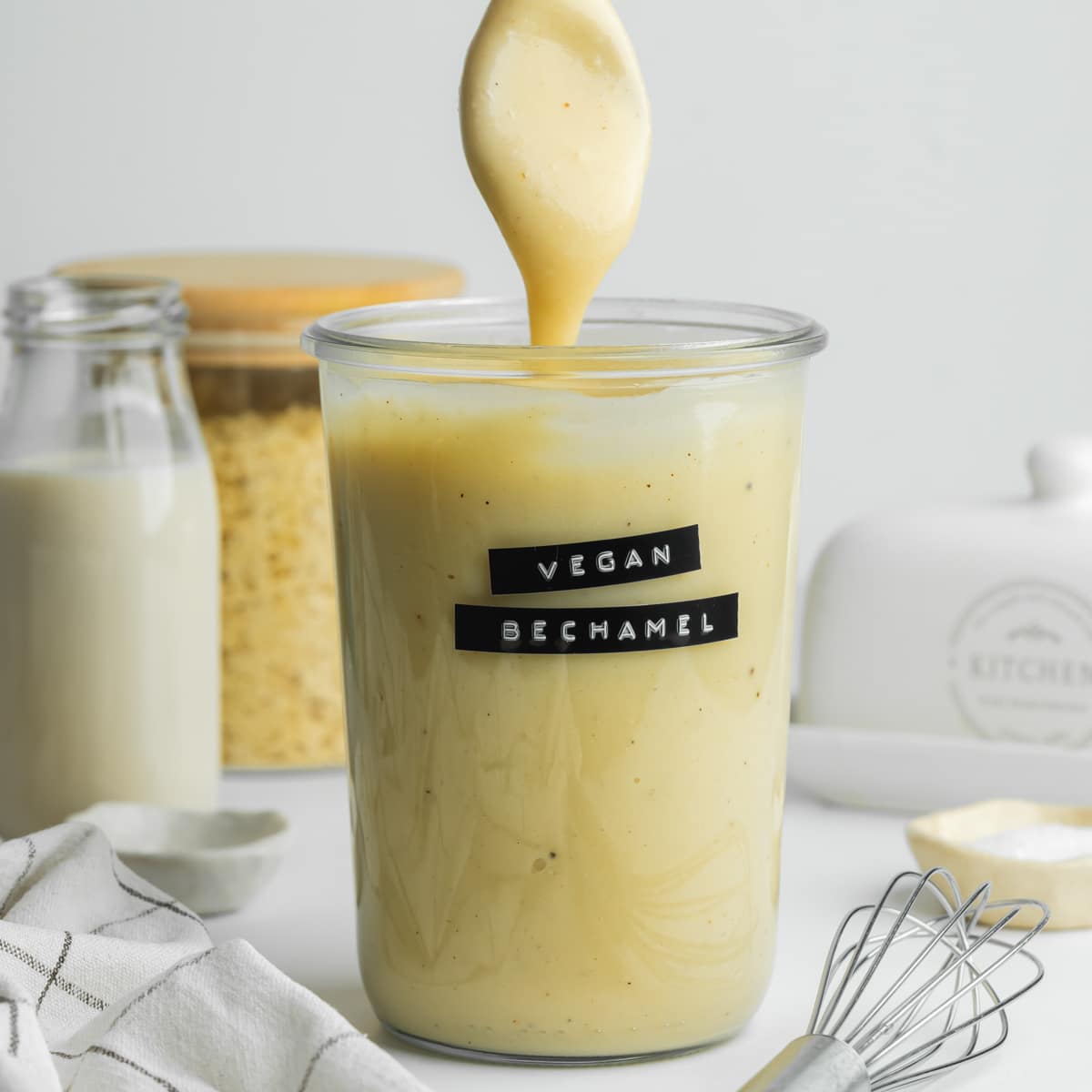 a jar of vegan bechamel with a spoon showing the thick consistency.