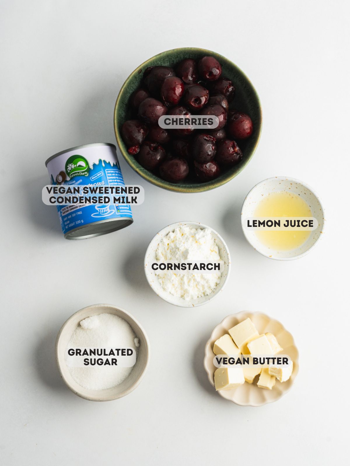 ingredients for cherry curd measured in bowls on a white surface.
