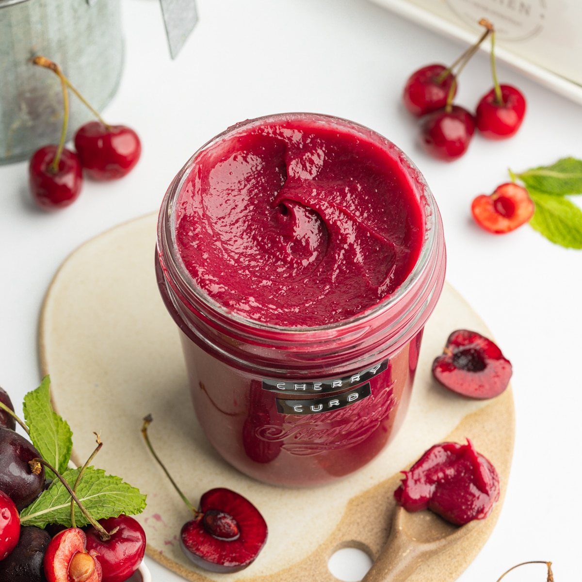 a jar of homemade cherry curd with fresh cherries scattered around it.