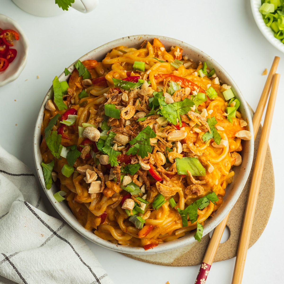 a bowl of creamy peanut butter noodles topped with scallions, peanuts, and fresh cillantro.