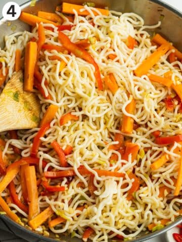 cooked noodles being mixed into the cooked veggies in a pan.