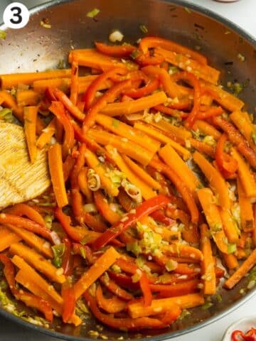 fried green onion, garlic, ginger, carrot, and red pepper in a saucepan.