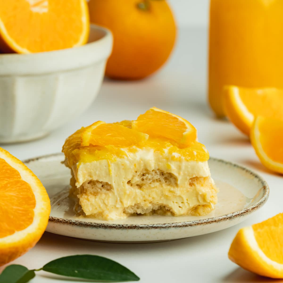 a slice of orange tiramisu with fresh oranges and orange juice in the background.
