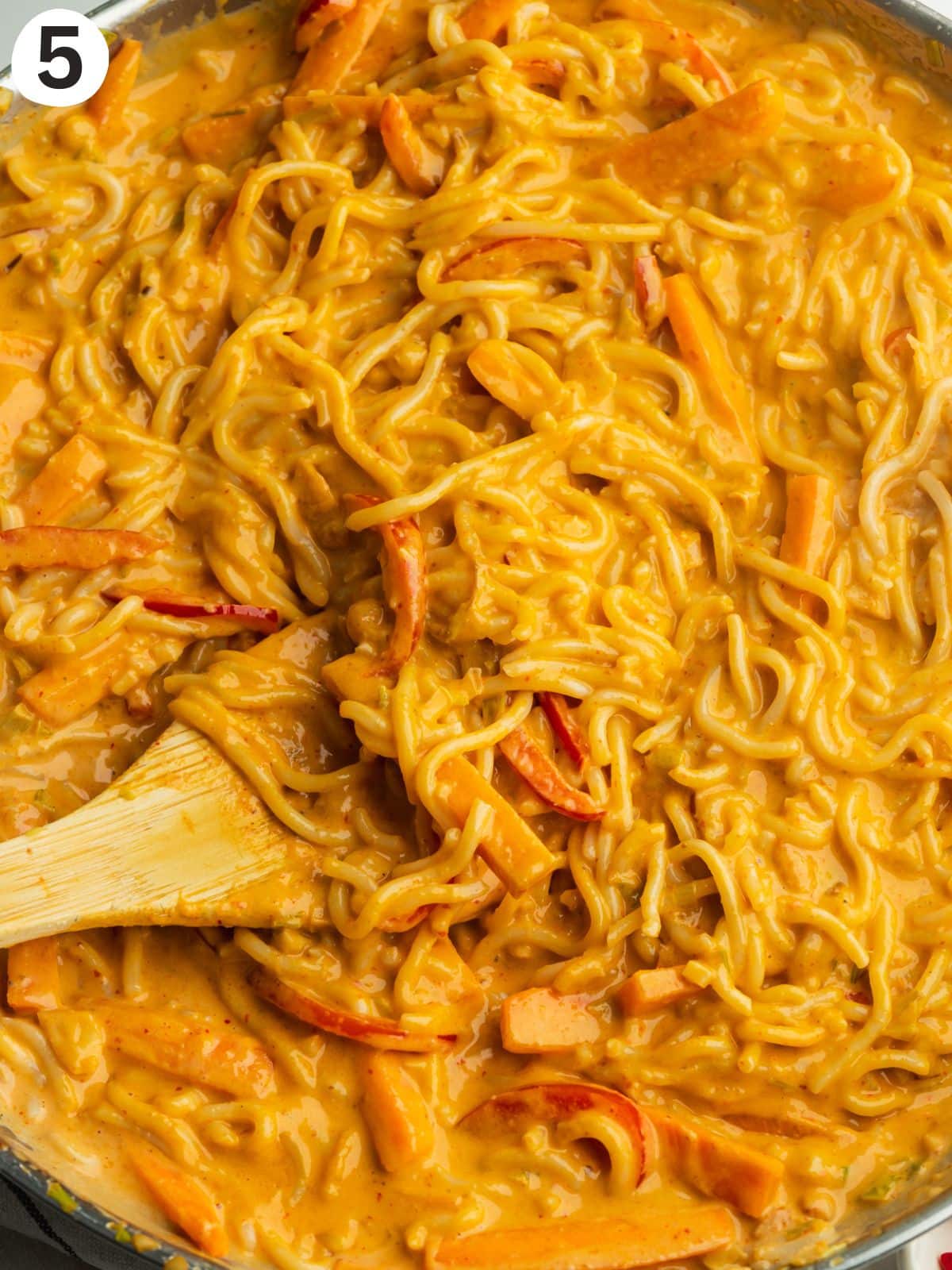noodles and veggies in a saucepan with a creamy peanut butter curry sauce.