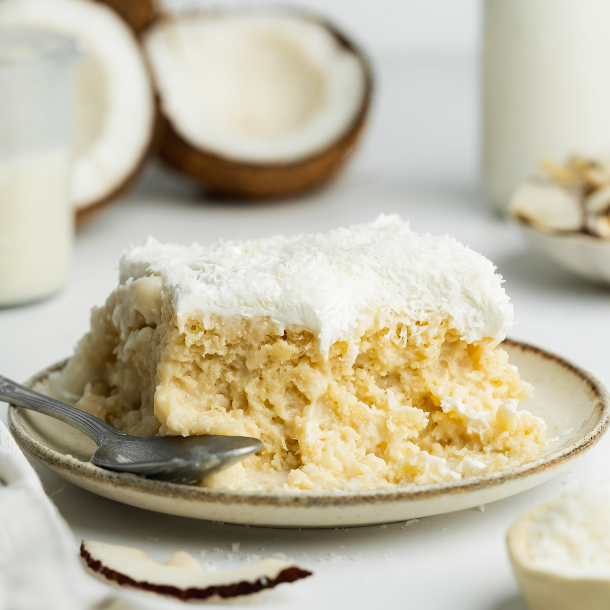 a slice of coconut tres leches on a plate with fresh coconuts in the background.