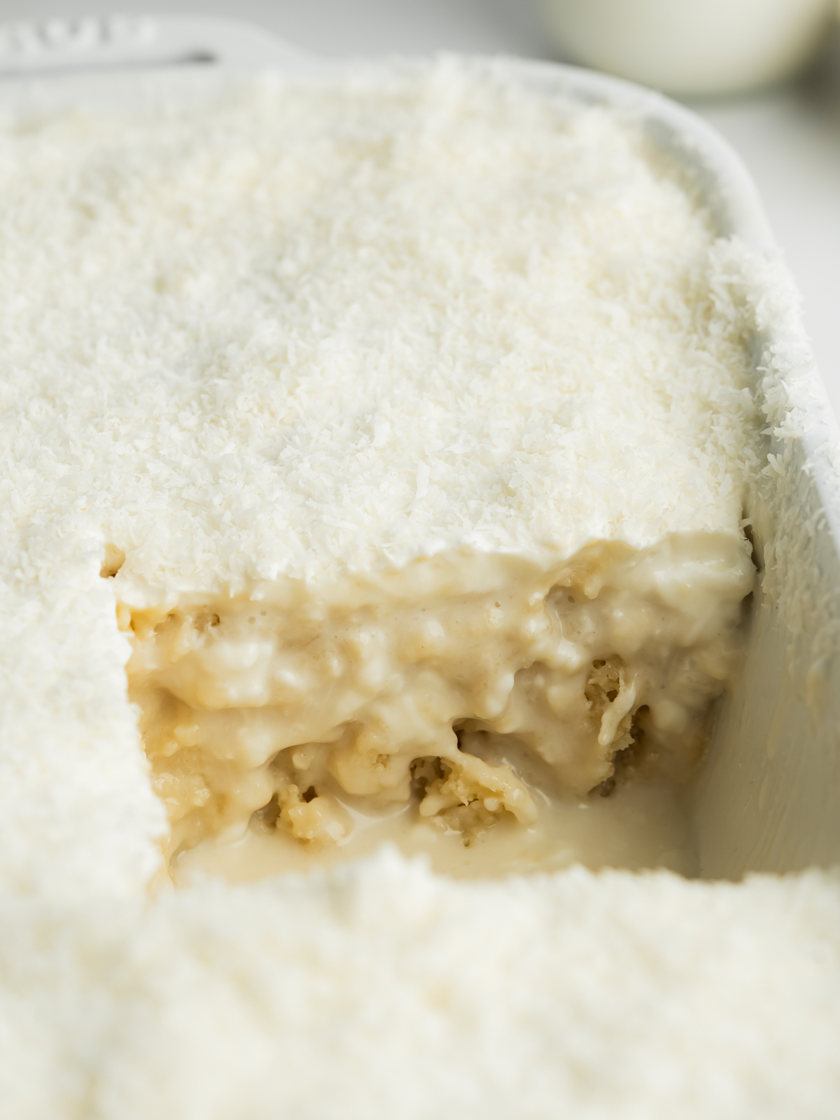 coconut tres leches in a staub dish with a slice taken from it.
