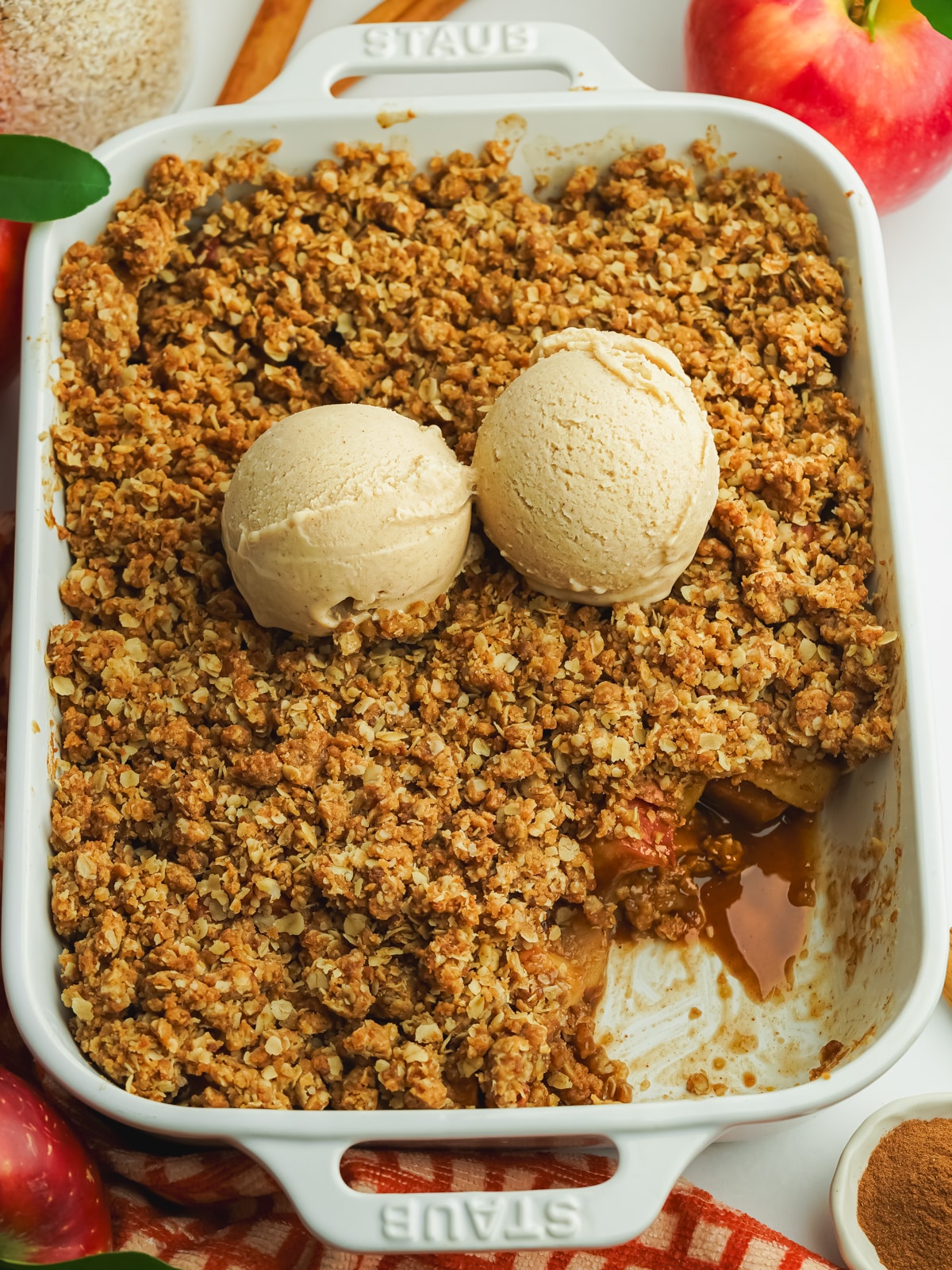 a staub pan filled with apple crisp and topped with 2 sccops of cinnamon ice cream.