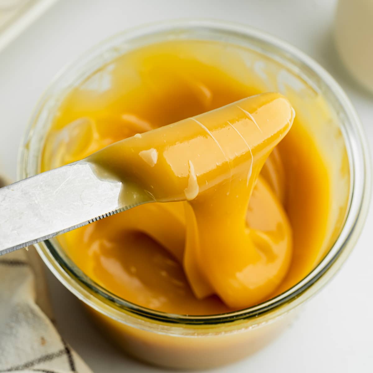 a jar of one ingredient vegan dulce de leches with a knife showing the thick consistency.