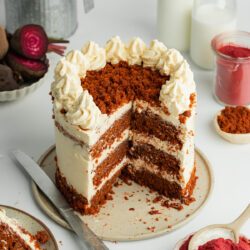 a triple layer vegan red velvet cake on a ceramic plate with a couple of slices cut from it.