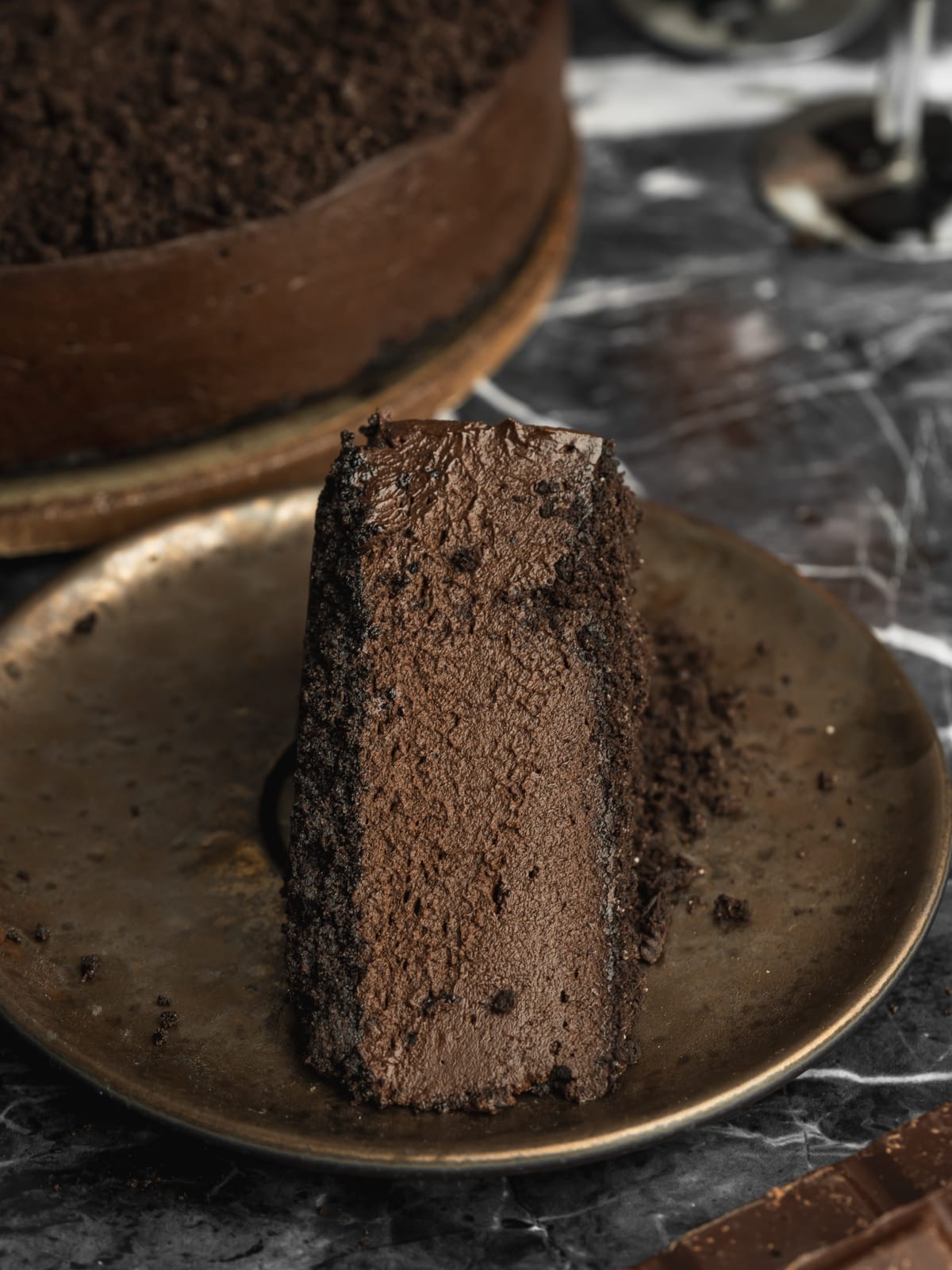Close-up slice of vegan dark chocolate Halloween cheesecake with a creamy chocolate filling and Oreo cookie crust.