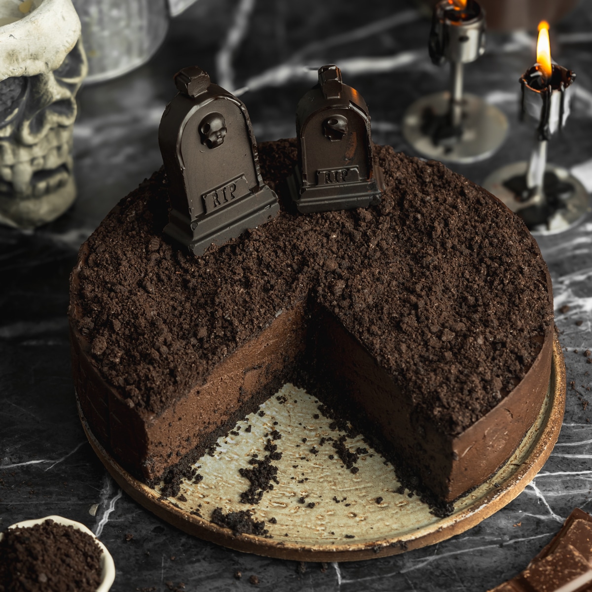 a halloween themed cheesecake with crushed oreos and chocolate grave stones on top.